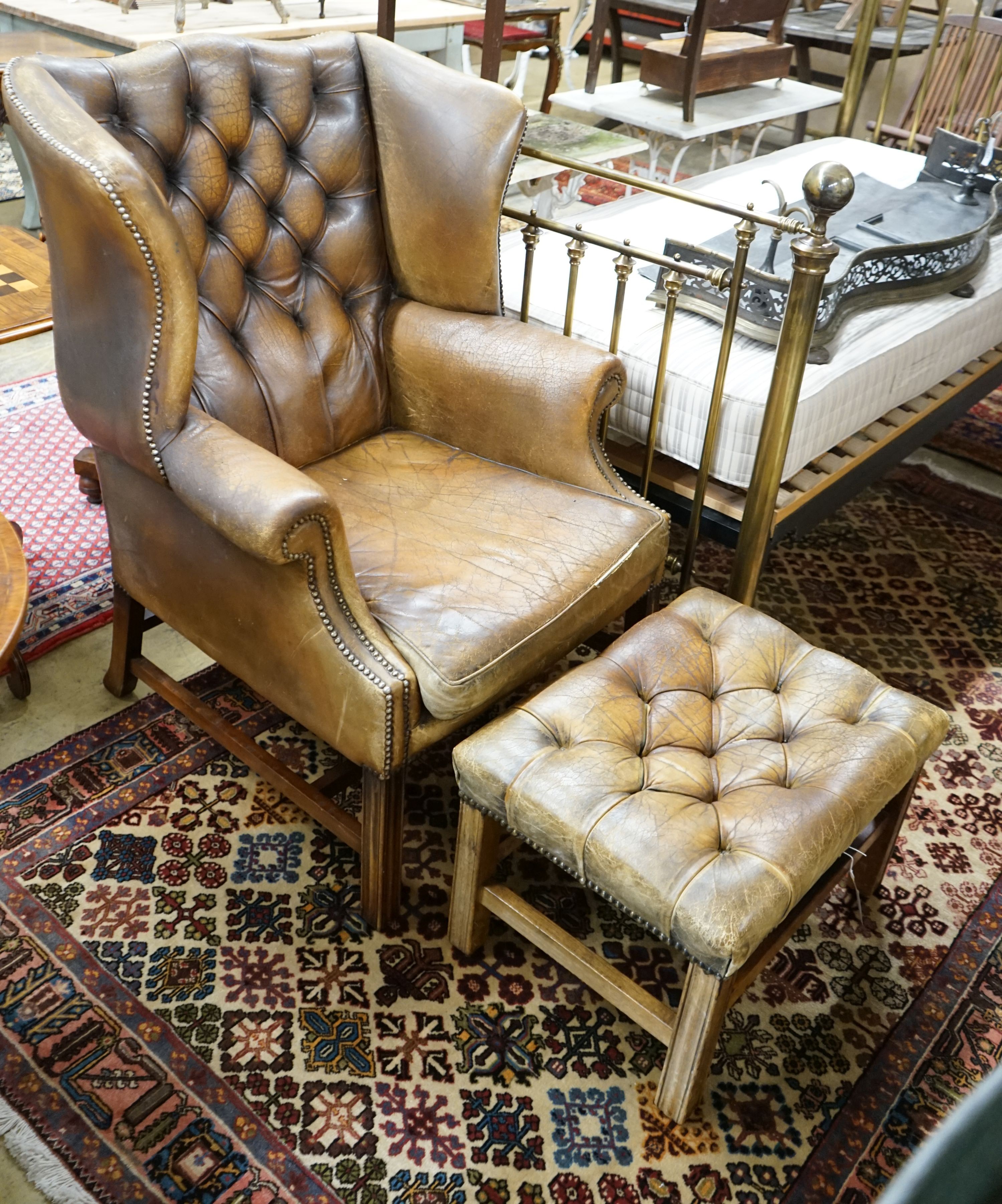 A leather wing armchair upholstered in buttoned brown leather, width 82cm, depth 77cm, height 110cm together with a similar foot stool